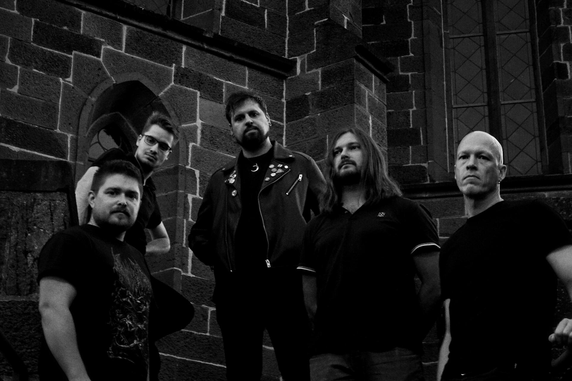 Our Visit To The Moon band photo September 2023 Black and white photo of the five male bandmembers of Our Visit To The Moon in dark clothing posing in front of a church wall